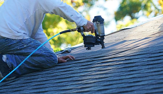 handyman using nail gun to install shingle roof
