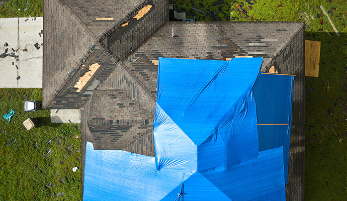 An aerial view of a house roof partially covered with a large blue tarp