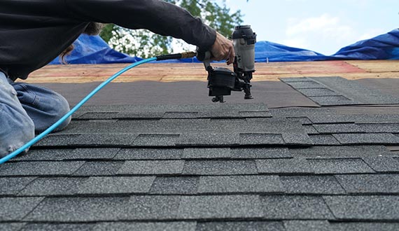 man using nail gun to install shingle to repair roof
