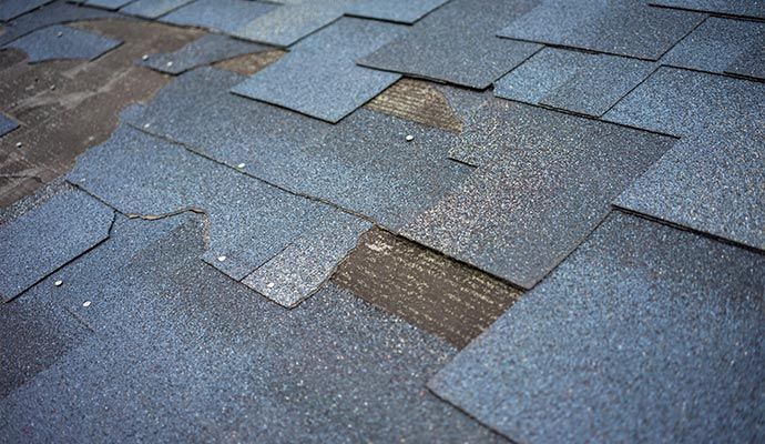 A close-up of a damaged roof with several missing and broken shingles