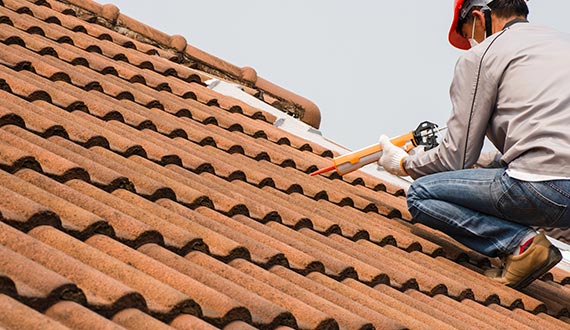 technician man hand using glue gun with silicone adhesive on the roof repair and building construction